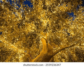 Golden tree leaves with LED twinkle lights or icicle lights. Big gold tree decorated with yellow lights to celebrate seasons greetings, holiday season of Christmas and new year. Night shot.