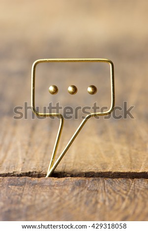 Golden tweet or remark. Blank speech bubble made of gold wire on rustic or grunge wood . Shallow depth of field.