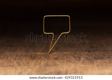 Golden tweet or remark. Blank speech bubble made of gold wire on rustic or grunge wood ready for inserting text. Dark background. Shallow depth of field.