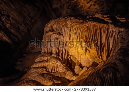 Golden and warm light illuminates the dramatic stalactite pillars and smooth stone textures of a deep subterranean cavern.