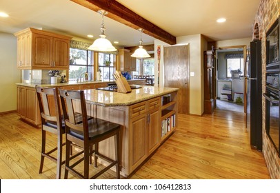 Golden Warm Wood Kitchen With Large Island And Back Appliances.