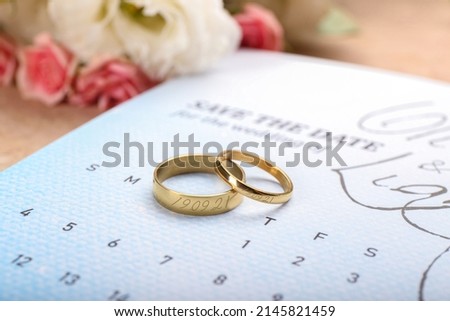 Golden wedding rings with engraved date of ceremony and calendar on table, closeup