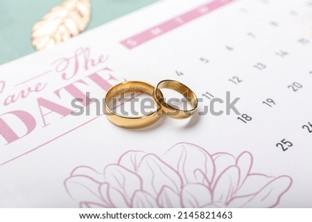 Golden wedding rings with engraving and calendar on table, closeup