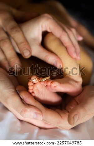 Golden wedding rings on tiny  newbornbaby's feet and toes in hands or palms of new parents, mom and dad 