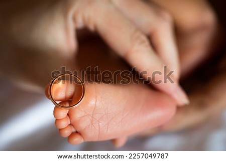 Golden wedding rings on tiny  newbornbaby's feet and toes in hands or palms of new parents, mom and dad 