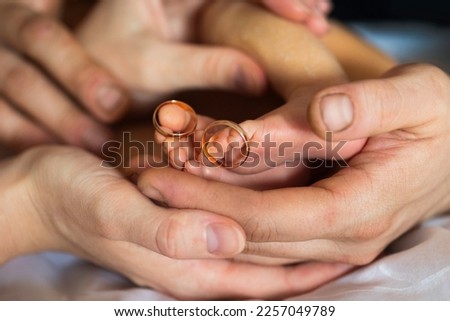 Golden wedding rings on tiny  newbornbaby's feet and toes in hands or palms of new parents, mom and dad 