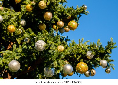 Golden And White New Year Decorations And Garland On A Branches Of Artificial Christmas Tree Outdoors On A Blue Sky Background At Sunny Summer Day. No People, No Snow. Copy Space.