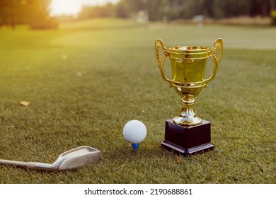 Golden winner cup with golf ball and golf club on green grass on golf course. Golf competition, sport championship