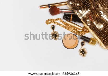 Golden woman accessories. Make up pieces, jewelry and shiny purse. Top view.