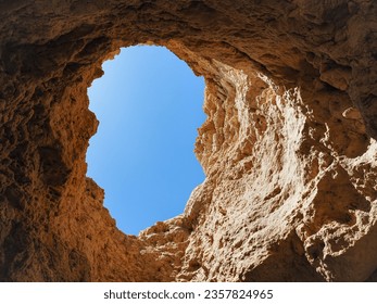 Golden yellow cave, with steep cliff and round hole on the top, with the blue sky view. Beautiful 