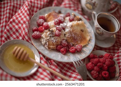 Golden-brown cottage cheese pancakes served with fresh raspberries, lightly dusted with powdered sugar. The plate is accompanied by a vintage teapot, a cup of tea, and a red gingham cloth, creating a  - Powered by Shutterstock