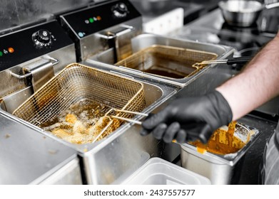 golden-brown fried chicken wings being lifted from a commercial kitchen fryer. The stainless steel fryer contains several crispy wings. A person’s gloved hand holds the basket handle - Powered by Shutterstock