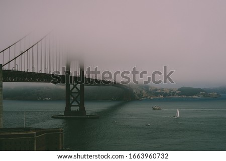 Goldengate bridge covered in mist with boat passing underneath