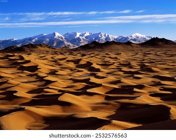 Golden-hued dunes stretch across the foreground, with rugged snow-capped mountains under a vivid sky, showcasing a stunning natural contrast. - Powered by Shutterstock