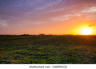 Golden-yellow setting sun and colorful cloudy sky over a newly mowed meadow. Rural place,  close to Rotterdam, Netherlands.