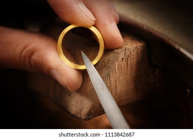 goldsmith hand holds a golden ring and works on it with a metal file, close up with copy space,  focus, narrow depth of field