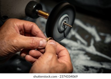 Goldsmith polishing a gold ring jewel in his jewelry workshop. Jeweler hands working in his craftwork studio. - Powered by Shutterstock