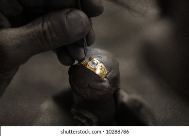 Goldsmith working on an unfinished 22 carat gold ring with big diamond with his hard working hands on grunge paper background - Powered by Shutterstock