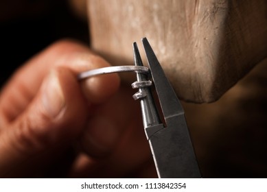 goldsmith wrap silver wire with pliers in a spiral for small chain rings, macro shot with blurry hand in the background, copy space, selected focus, very narrow depth of field - Powered by Shutterstock