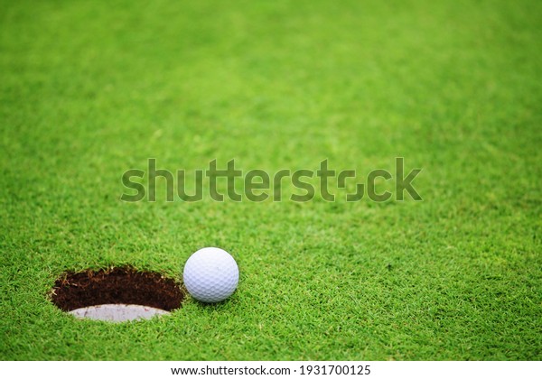 Golf ball\
close to hole, on lip of cup on green of golf course background\
with copy space for text\
banner