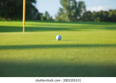 Golf Ball Close Up Low Angle View On A Green With Pin In Late Afternoon Sunlight