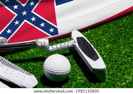 Golf ball and club with flag of Mississippi on green grass. Golf championship in Mississippi