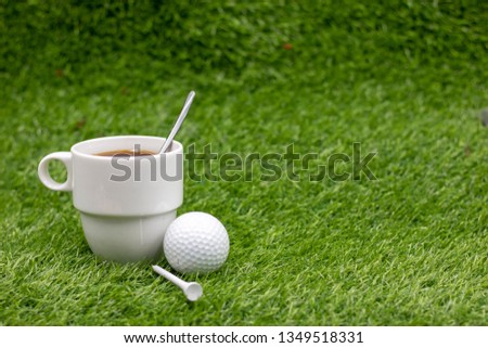 Golf ball with cup of tea on green grass, drink for golfer at club house