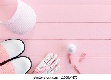 Golf ball, golf glove, tees, golf shoes and golf visor  on a wooden surface in pink, top view, ladies day