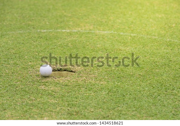 Golf\
ball on the lawn in the hole green golf pro player putting golf\
ball into hole , hand , flag in hole and Golf car\

