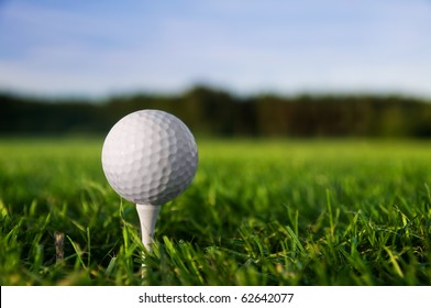 Golf Ball On Tee. Green Grass, Blue Sky.