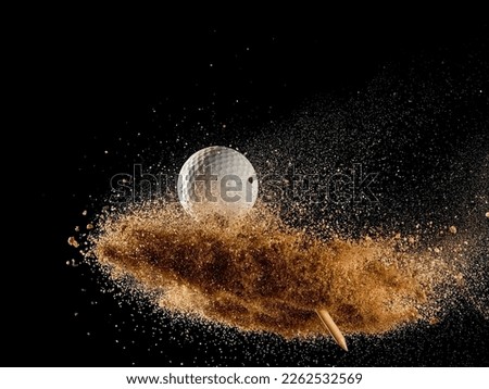 Golf ball and wooden tee flying in cloud of sand on black background