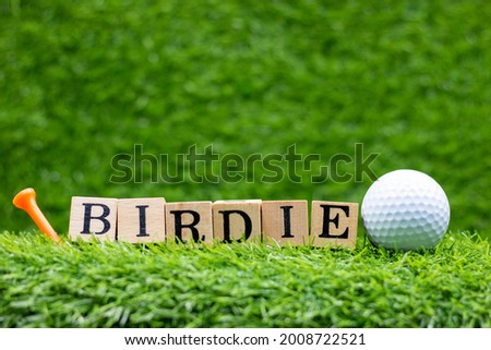 Golf ball with word Birdie and tee on green grass background. Birdie: A hole played one stroke better than the expected standard (one under par).