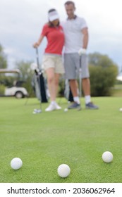 Golf Balls On Green With A Golfing Couple In Background