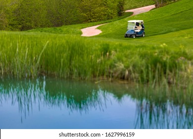 Golf Buggy On The Bank Of The Lake, No People, Sunny Day And Green Grass.