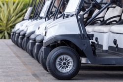  Golf Cars In A Row Outdoors On A Golf Course. A Row Of Empty Golf Carts On A Course. Golf Course Carts Cars At Luxury Resort Sport Venue.All Lined Up Ready For A Tournament On A Course. 