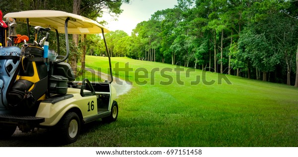 Golf cart or car on golf course. Looking see\
beautiful layout and fairway. Beautiful Road for cart to drive.\
Morning sky and cloud. Equipment and bag are put in ready for\
golfer to player in field