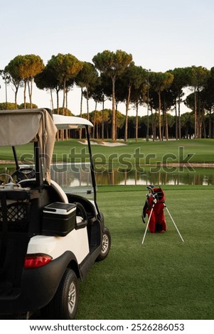 Golf cart and red bag with golf clubs staying on the green golf course front of luxury landscape 