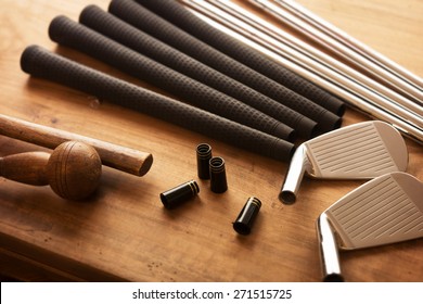 Golf club making. Golf club components on a work desk or work bench. grips, shaft, ferrules  and, iron head.Focus is on black ferrule parts. Shallow depth of field.