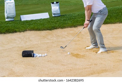 Golf Coach Hitting Golf Ball. No Face, Sand Splashing.