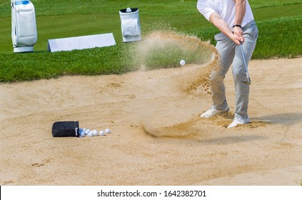 Golf Coach Hitting Golf Ball. No Face, Sand Splashing.