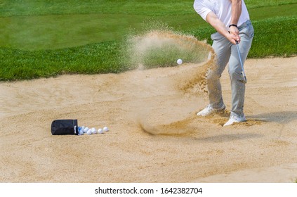 Golf Coach Hitting Golf Ball. No Face, Sand Splashing.