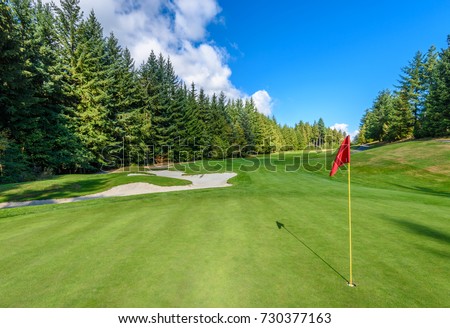 Golf course with gorgeous green, sand bunker and golf flag and real estate on background.