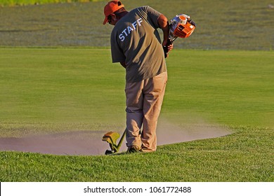 A Golf Course Maintenance Worker Trimming Grass Near A Sand Trap On A Local Golf Course