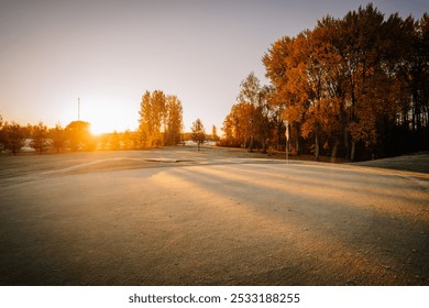 A golf course at sunrise with frosty grass, long tree shadows, and a flagstick, surrounded by autumn foliage. - Powered by Shutterstock