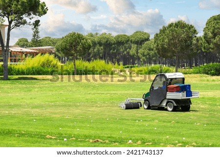 Golf course and a vehicle collecting golf balls. Ballpicker on driving range of golf club