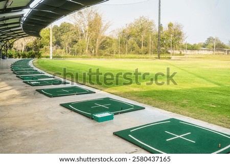 Golf driving range with multiple tee areas under shaded canopy, surrounded by lush green grass for leisure activity, sport practice