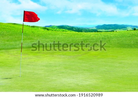 Golf field. Green grass against the background of the sea shore and the blue sky. Signal flag for the hole on the golf course