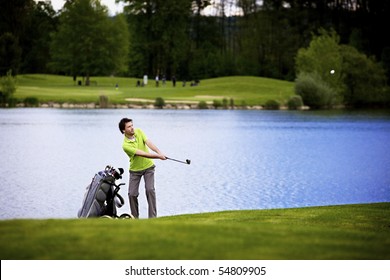 Golf Player Pitching Golf Ball At Lake With Ball In The Air.