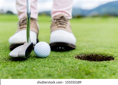 Golf player at the putting green hitting ball into a hole  - Powered by Shutterstock