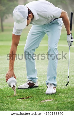 Golf player repairing divot with sand on fairway